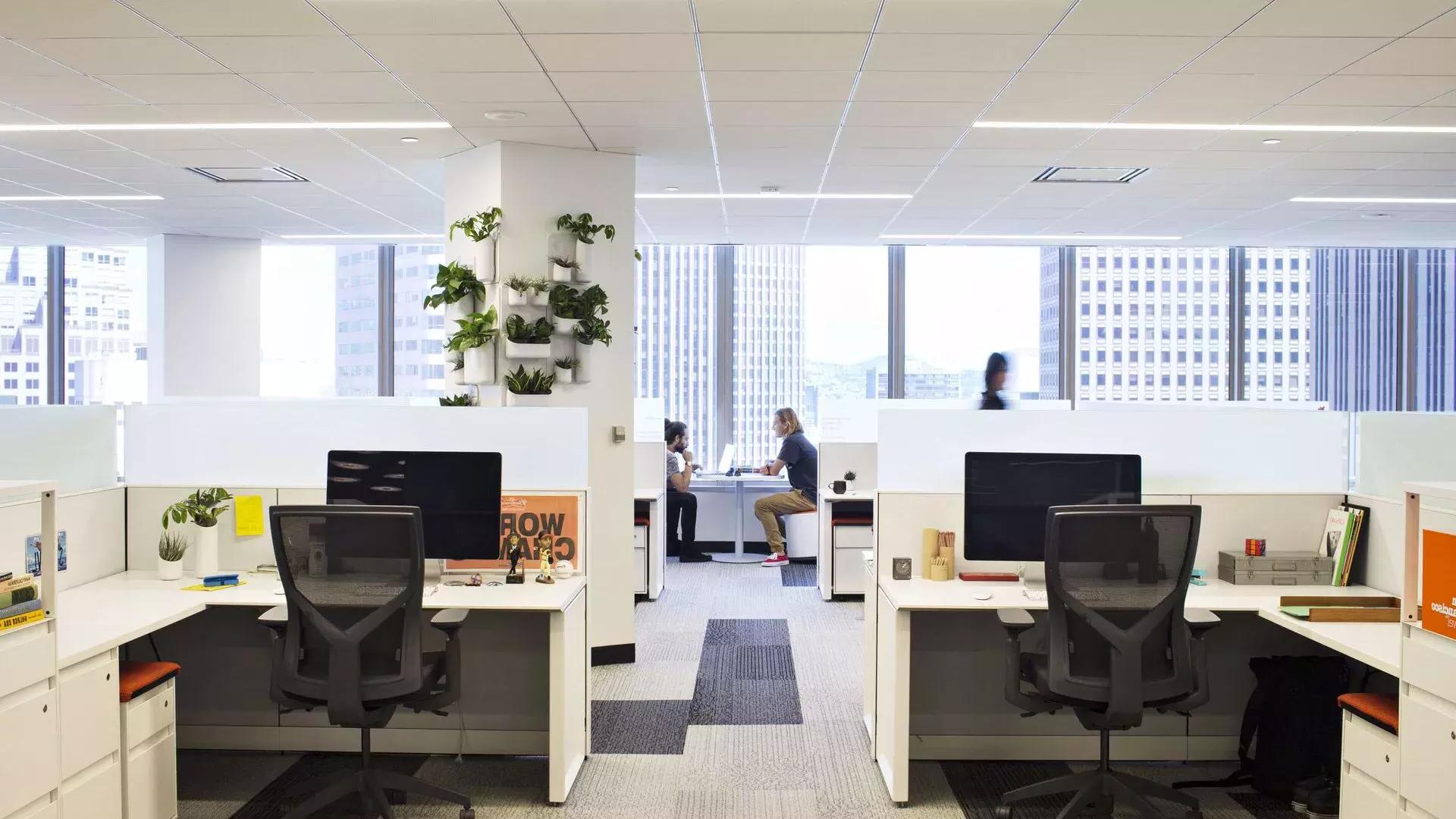 Interior scene at an office building in San Francisco, 前景有几张桌子，两个人在大窗户前的一张桌子前工作.