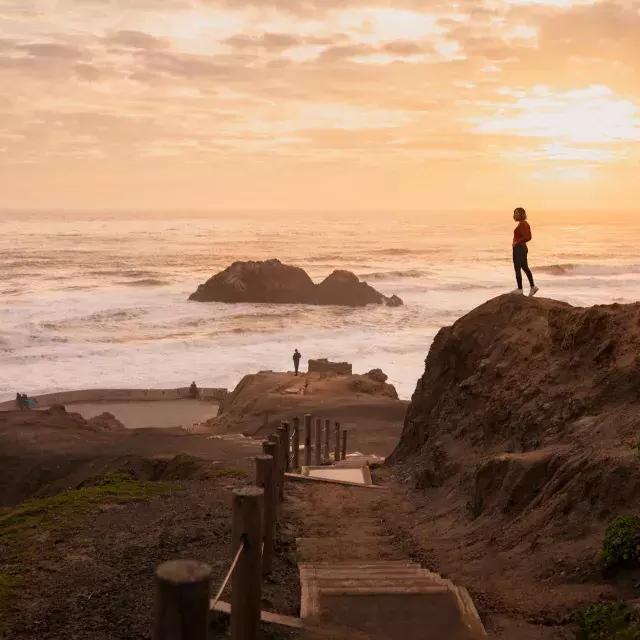 Two people st和 on rocks overlooking the ocean at Sutro Baths in San Francisco.